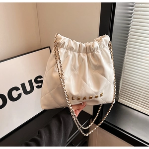 Detail of white quilted bucket bag featuring a gold metal brand logo and chain strap