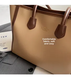 Detail of soft beige tote bag with brown handles and gold logo on textured fabric