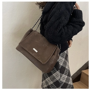Détail du sac cabas marron foncé mat avec bandoulière chaîne et plaque logo métal