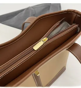 Close-up of smooth gold metal zipper and white stitching on two-tone tote bag