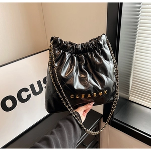 Detail of black quilted bucket bag featuring gold CLEAR logo and chain strap
