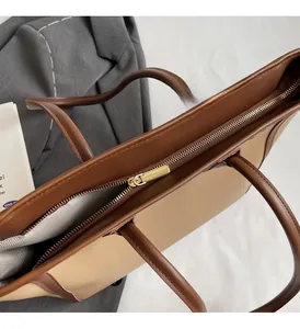 Detail view of large tote bag with brown faux leather trim and golden zipper closure