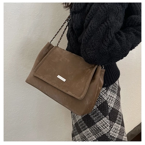 Détail d'un sac cabas marron en cuir mat avec plaque argentée et bandoulière chaîne