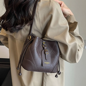 Sac seau en cuir matelassé marron avec cordon et détails dorés, porté par un modèle