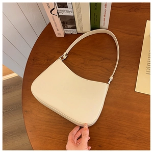 Top view of a cream minimalist underarm bag on a dark wood table with stylish books