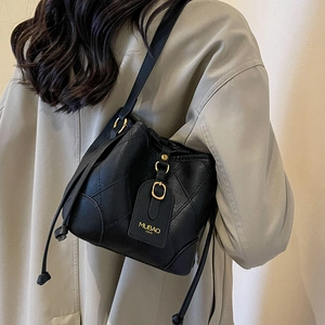 Sac seau chic en cuir noir matelassé avec garniture dorée porté par un mannequin