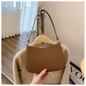 Brown leather half-moon shoulder bag hanging on a wooden hanger in a cozy setting