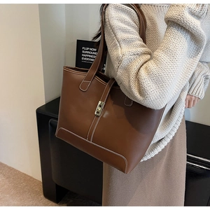 Detail of caramel brown tote bag featuring white contrast stitching and gold metal twist lock
