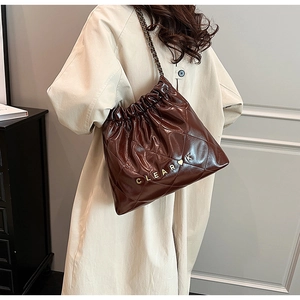 Detail of dark brown quilted leather bucket bag with chain strap and metal letters