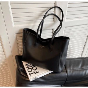 Close-up of matte black leather tote bag featuring gold logo and slim shoulder straps