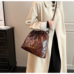 Detail of dark brown quilted bucket bag with gold letter logo and chain strap on shoulder