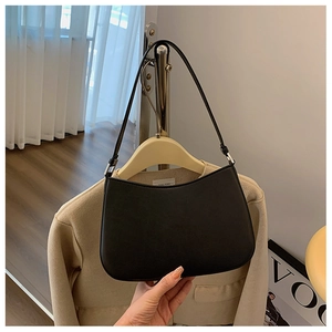 Detail of a black matte leather underarm bag with silver buckle on a beige coat hanging