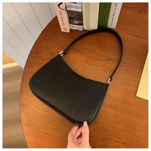 Close-up of a minimalist black leather hobo bag with silver metal buckles on a wooden table