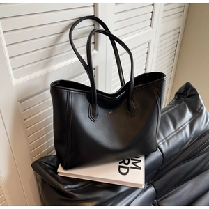 Detailed close-up of a matte black tote bag with gold logo and dual thin shoulder straps