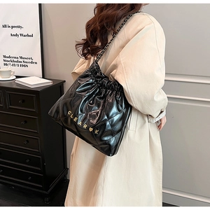 Detail of black quilted leather bucket bag with chain strap worn by a model in beige coat