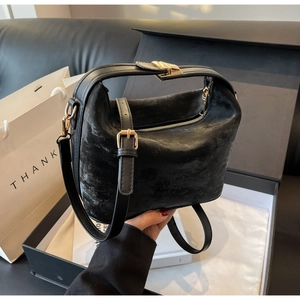 Détail d'un sac à main noir mat avec boucles dorées et bandoulière dans son emballage cadeau