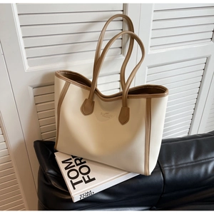 Detail of off-white tote bag with brown straps on a black leather sofa with book