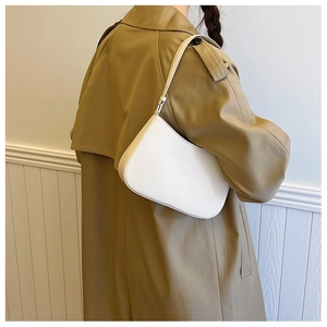 Minimalist white leather hobo bag with sleek curved lines worn over a khaki trench coat