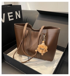 Detail of a dark brown leather tote bag with white stitching in a luxury gift box packaging