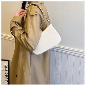 Side view of cream leather underarm bag with thin shoulder strap on model's outfit