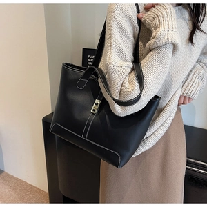 Detail of black leather tote bag with white contrast stitching and gold square swivel lock