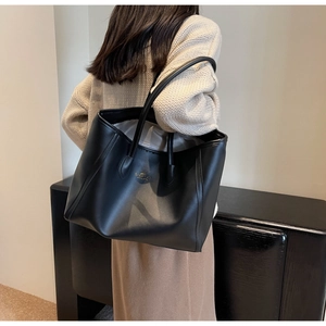 Close-up of black leather tote bag with gold logo and slim handles for commuting