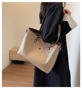 Detail of a minimalist beige tote bag with brown straps and metal rivet accents