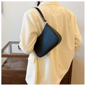 Rear view of a black matte leather hobo bag worn on the shoulder with a beige suit