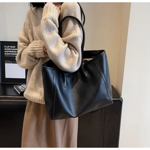 Close-up of black leather tote bag with gold logo and long shoulder straps for daily commute