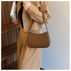 Detail view of a brown faux leather underarm bag held by a model in a blazer