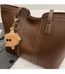 Detail of brown faux leather tote bag with white contrast stitching and plush charm