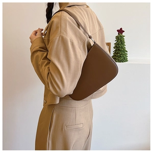 Brown underarm bag shown on a model wearing khaki casual wear against a minimalist wall