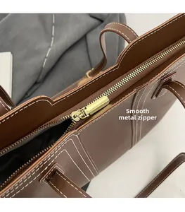Detail of smooth gold zipper and white stitching on brown leather tote bag