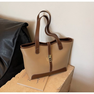 Detail of contrast stitching and golden clasp on a beige and brown leather tote bag