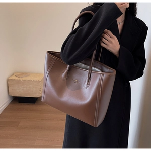 Detail of dark brown leather tote bag with gold logo and long shoulder handles