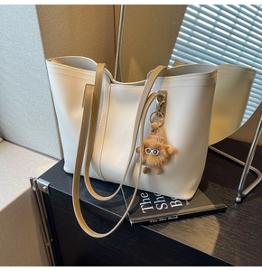 Detail of cream tote bag with brown straps and a cute plush monster charm on a shelf