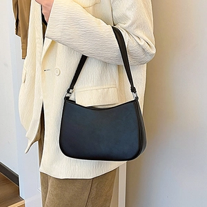 Minimalist black crescent underarm bag with silver hardware on a model in a beige blazer