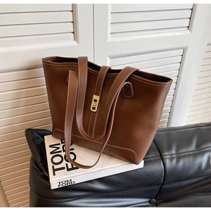 Detail of a brown leather tote bag with white contrast stitching and a gold swivel lock