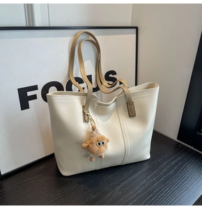 Detail of a minimalist beige leather tote bag with brown straps and a plush monster charm