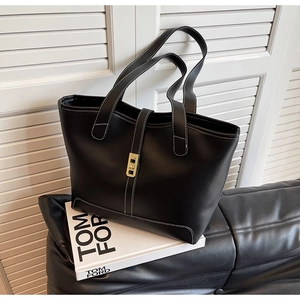 Detail of black leather tote bag featuring contrast white stitching and gold swivel lock