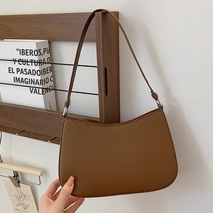 Brown leather minimalist crescent underarm bag with silver chain strap on a white wall