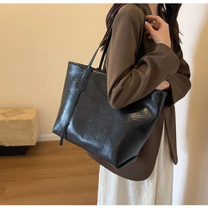 Detail of a large black tote bag featuring vintage pleated texture and slim shoulder straps