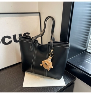 Detail of black tote bag with white contrast stitching and a plush lion charm