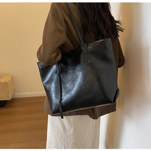 Detail of black faux leather tote bag showing glossy crinkled texture and slim shoulder strap