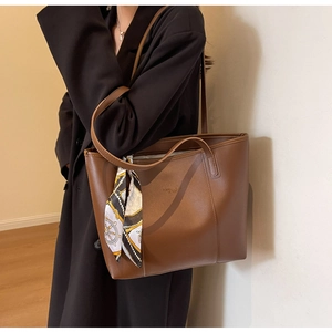 Brown leather tote bag with printed scarf detail shown on a shoulder in a minimalist setting