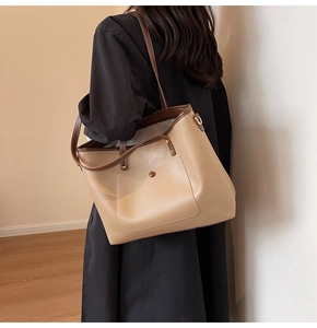 Detailed side view of a large beige tote bag with brown trim worn on the shoulder
