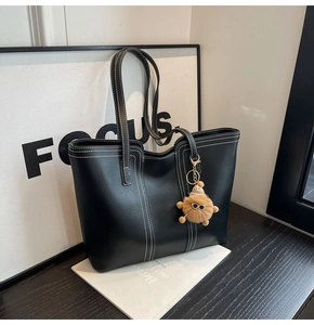 Close-up of black leather tote bag with white contrast stitching and brown plush charm