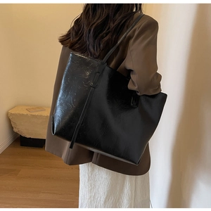 Close-up of a black glossy wrinkled leather tote bag showing texture and shoulder strap