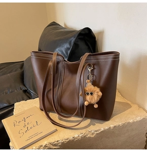 Detailed close-up of brown tote bag with contrast stitching and plush pompom charm