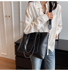 Macro shot of black leather tote bag featuring contrast white stitching and wide strap